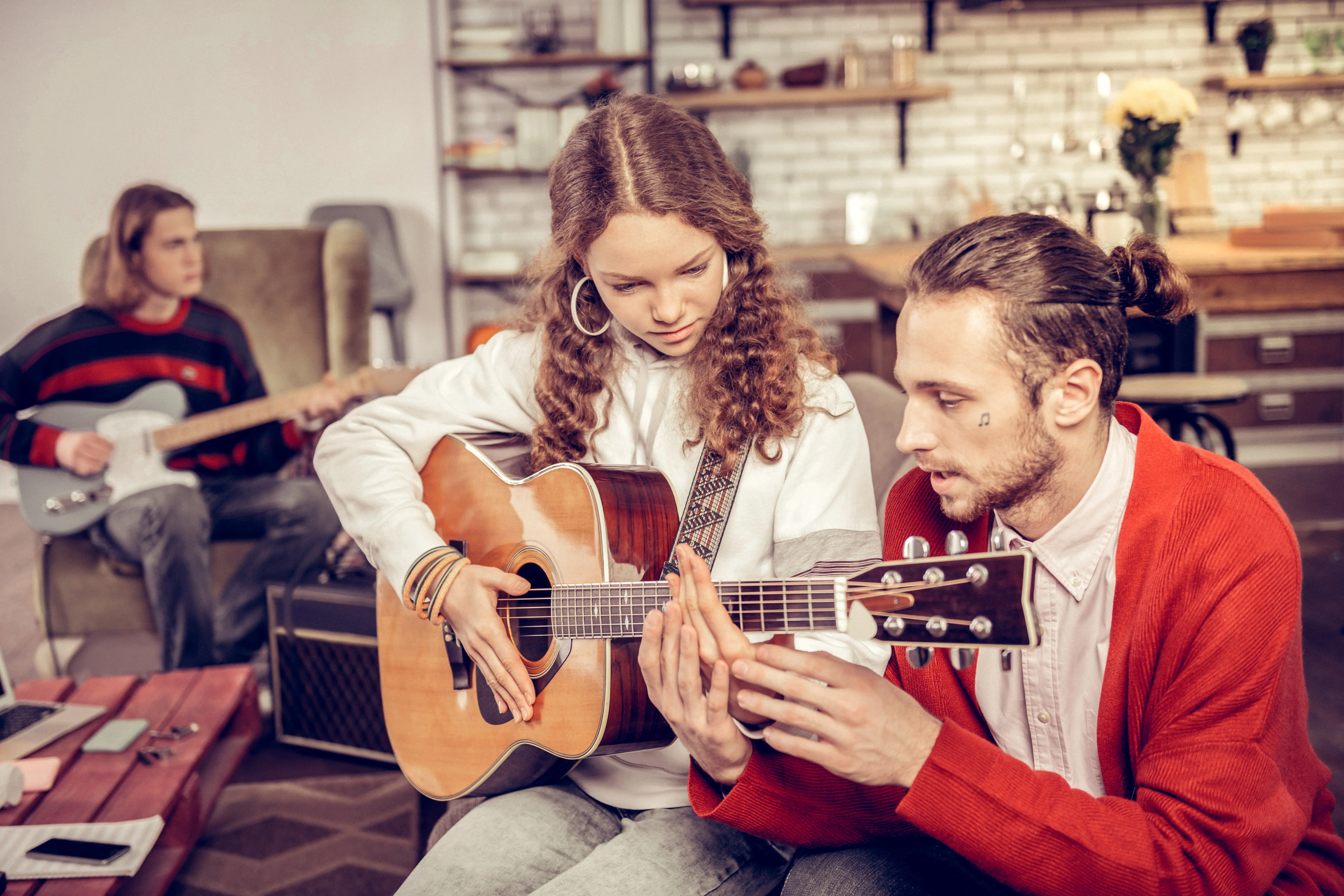 Unterricht für Teenager. Ein bärtiger Musiklehrer bringt Teenagern im Wohnzimmer das Gitarrespielen bei.